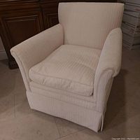 Front view of beige corduroy small armchair showing cushioned seat, flared backrest and rolled arms.