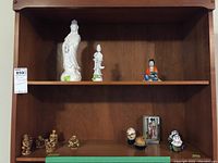 Display shelf with various Asian figurines of mixed materials including porcelain and metal, totaling thirteen pieces forming the lot