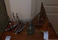 Wide view of four decorative boat models with varying wooden and metal materials and one glass decanter with cork.
