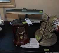 Photo showing Bombay Co quartz anniversary clock in wood and glass, gray desk lamp, and sculpture figurine