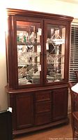 Full front view of buffet and hutch showing glass display with items inside and wooden base with drawers and cabinets.