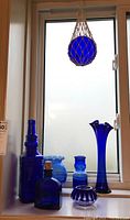 Seven cobalt blue glass pieces displayed on a windowsill with a hanging glass ball above