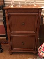 Front view of wood file cabinet showing two drawers with metal handles and decorative column corners.