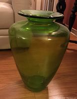 Side view of the large green glass floor vase showing the full shape and size relative to nearby furniture.