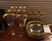 Set of assorted clear glass stemware with gold rimming and matching plates with gold rims on a wooden table.