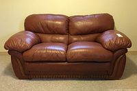 Front view of brown leather loveseat with plush cushions and wood accents