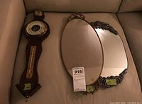 Three items on a couch: two wall mirrors and one wood barometer with thermometer and dial, all arranged closely for clear view.