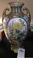 Full view of the hand painted urn vase showing the floral artwork, ornamental gold handles, and detailed neck and base patterns.