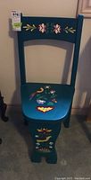 Front view of small teal wooden chair with floral decorative tole painting on backrest, seat, and legs.