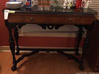 Full view of the wood side table showing the dark finish, drawer with ring pull handles, carved edges, and turned legs.