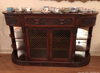 Front view shows ornate sideboard cabinet with decorative carved floral motifs, three drawers above, two doors with wire mesh, and open shelving at sides.