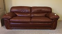 Front view of three-seat brown leather sofa with wood trim along base