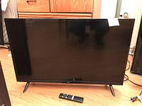 Full view of the TCL 32 inch TV with remote in front on wooden floor.