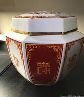 Side view of octagonal porcelain urn with red panels and gold E II R monogram surrounded by decorative gold detailing.