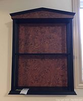 Front view of wall hanging shelf showing peaked top, wood grain back panel and two shelves.