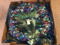 Wreath wrapped in black plastic inside a cardboard box for protection during storage or transit.
