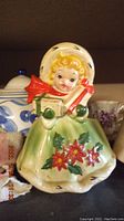 Front view of antique porcelain Christmas girl figurine with bonnet and gift.