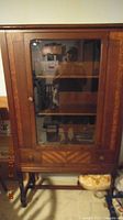 Full front view of the antique china cabinet showing glass door with inside shelves and drawer below. Walnut wood with wood grain visible. Brass or metal knobs on door and drawer.
