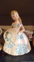 Front view of antique porcelain girl figurine showing blue floral dress and hat