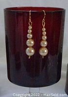Photo of pair of handcrafted antique natural salt water pearl earrings displayed hanging against a dark red container background.
