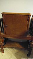Front view of the antique smokers table showing the closed door with knob and turned wooden legs ending in caster wheels.