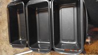 Top-view showing five black metal bread pans lined up side by side, rectangular shape with non-stick interiors