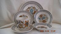 Photo showing 4 pieces of Broadhurst Seychelles ironstone dinnerware set including a coffee cup on its saucer and plates of different sizes, featuring floral Mediterranean motifs and graphic borders in orange, olive green, and turquoise colors.