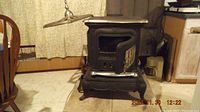 Front view of antique cast iron wood stove showing open hinged door and metal lid above.