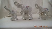 Three ceramic Asian lucky elephant figurines with trunks raised and floral decoration on a neutral backdrop.