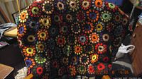 Photo of a large handmade crocheted afghan draped over a chair showing multi-colored circular flower motifs in various bright colors.