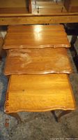 Top view of the three vintage wooden nesting tables showing water damage marks on the middle table's surface and scalloped edges on all table tops.