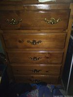 Front view of vintage solid wood tall boy dresser showing five drawers with brass handles and marks on the wood surface.
