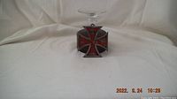 Photo of an Iron Cross shaped metal war medal with red enamel and crown detail with a clear glass goblet placed upside down on top of it.