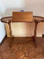 Front view of the antique writing desk with tilt top angled upward, showing metal trim along curved edges and carved wooden legs.
