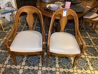 Pair of wooden arm chairs showing full front view, wood finish, and cushion seats on patterned carpet.