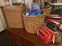 Photo of woven baskets, string lights boxes, gift wrapping supplies including gift bags and wrapping paper rolls, and beaded curtain packaged box on wooden dresser