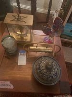 Photo showing brass wind-up mantel clock, brass kaleidoscope, butterfly necklace stand, ceramic covered bowl with lid on wooden table