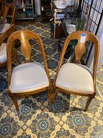 Pair of wooden dining chairs with white vinyl padded seats on a patterned floor.