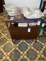 Frontal view of the coffee cart showing various glass and ceramic kitchenware on top and lower shelves.