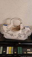 Front view of white ceramic transferware basket vase with black floral pattern on mixer surface