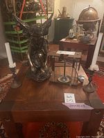 Photo showing the fairy statue centered with the pair of metal candlesticks flanking it on a wooden table, with the metal bar caddy placed behind the statue.