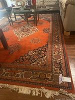 Full view of orange area rug under coffee table with floral medallion designs and fringed edges.
