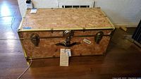 Full view of the wooden steamer trunk with metal hardware and leather handle on a wooden floor