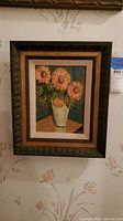 Full view of the framed painting showing pink flowers in a white vase on a table with dark blue background.