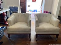 Pair of vinyl club chairs placed side by side on a hardwood floor near the entrance with natural lighting showing the overall condition and shape.