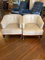 Pair of off-white vinyl club chairs on wheels, showing front and one side, both chairs visible, one needing trim repair on back