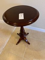 Front angled view of round cherry finish side table showing pedestal base and tabletop.