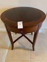 Front angled view of the round side table showing the drawers and cherry mahogany finish with inlaid border on tabletop.
