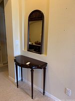 Full view of half moon demilune table and arched mirror on wall in niche.