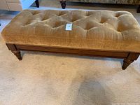 Front angled view of the upholstered bench showing tufting and wood frame with decorative front legs.